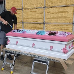 A worker decorates a pink-and-white casket with a TikTok symbol