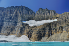 The picture shows a melting glacier and the pool of meltwater that has formed beneath it. The remaining snow is on a mountain. 