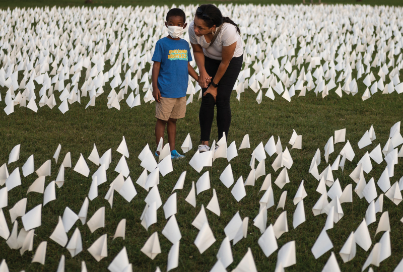 A Black woman leans to speak to a masked Black child amid a sea of small, white flags