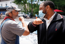 A Black man and a white man "high-fiving" each other with their elbows.