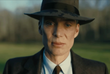 A photo shows a white man wearing a suit and a bowler hat looking into the camera seriously 