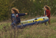 Two similar-looking small girls carry a raft together through a woody path