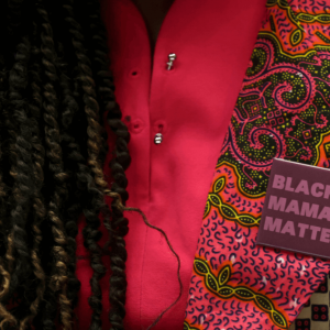 A woman with dreadlocks and a pink shirt wears a purple pin says "Black Mamas Matter"